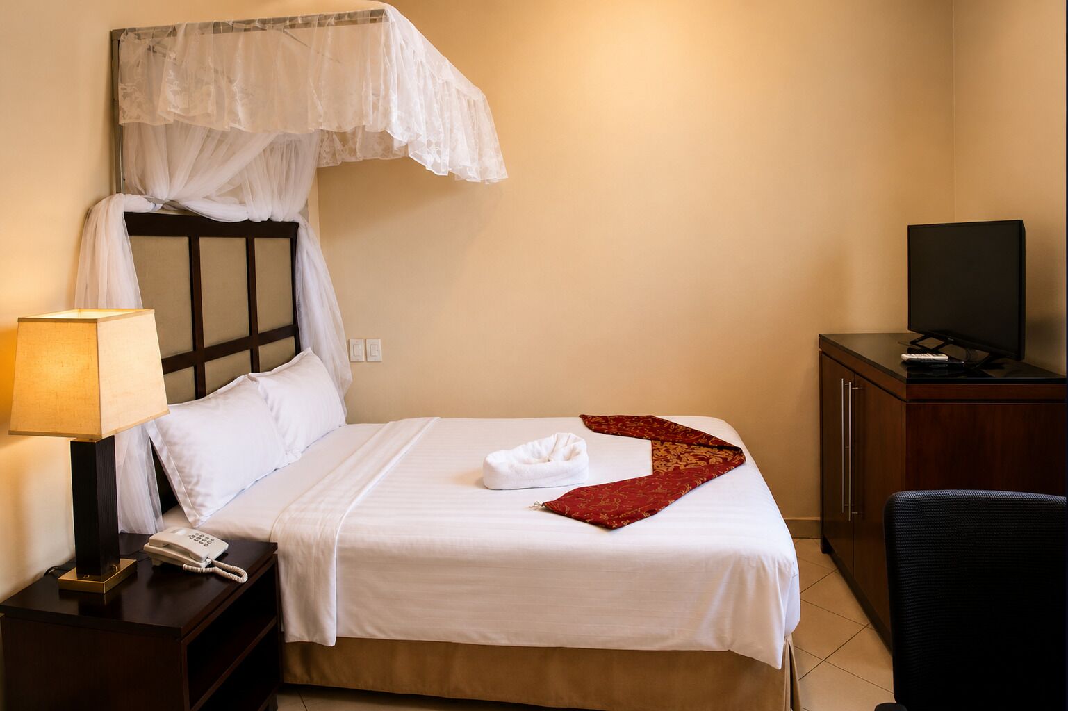 A hotel room with a bed, a bedside telephone, a television on a wooden cabinet, and a chair.