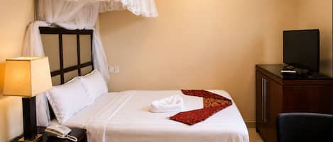 A hotel room with a bed, a bedside telephone, a television on a wooden cabinet, and a chair.