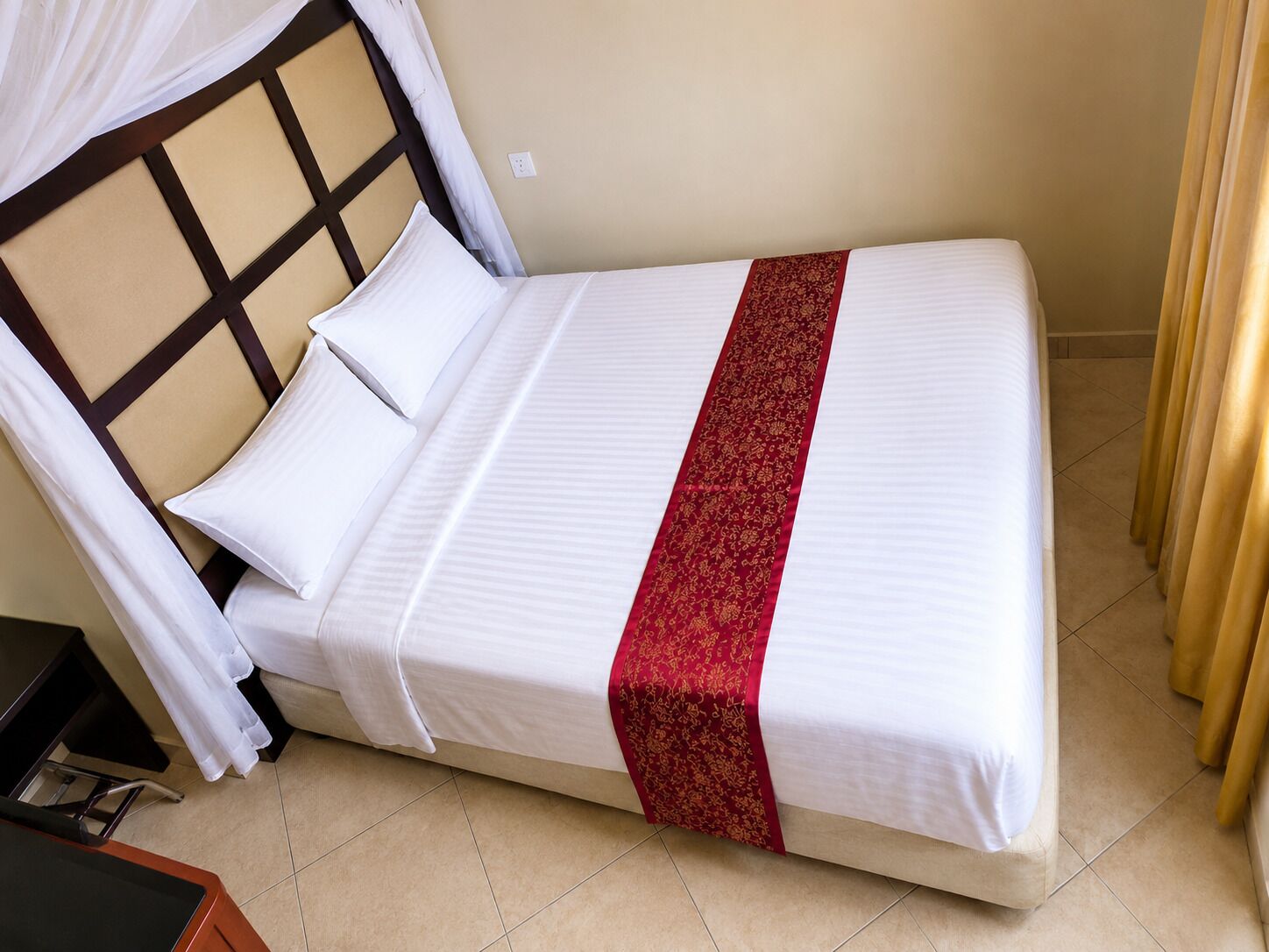 Una cama individual con cabecera, ropa de cama blanca y un detalle decorativo rojo.