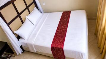 Una cama individual con cabecera, ropa de cama blanca y un detalle decorativo rojo.