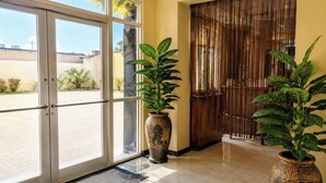 Entrada de hotel con puerta de vidrio, puerta de madera y dos grandes macetas.