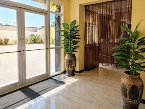 Entrada de hotel con puerta de vidrio, puerta de madera y dos grandes macetas.