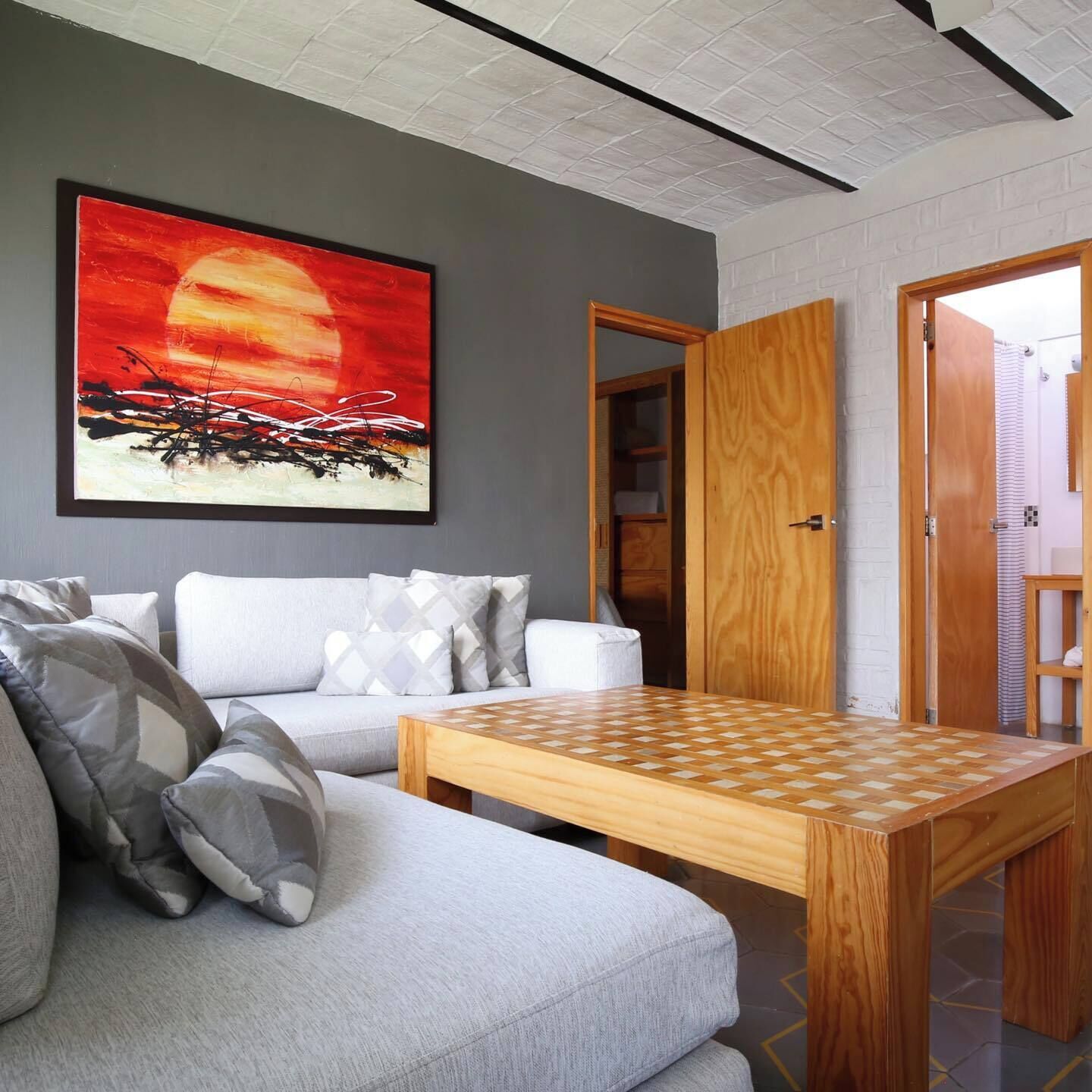 Un salon moderne avec un canapé gris, des coussins à motifs, une table basse en bois et un grand tableau abstrait accroché au mur.