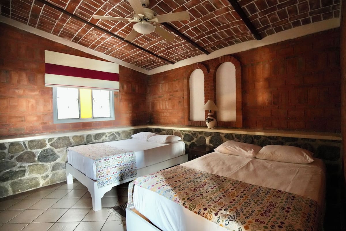 A room with two beds, a stone wall, a wooden ceiling, and a window with a view.
