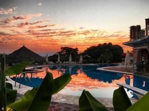 A swimming pool with a sunset view, lounge chairs, and a thatched-roof structure.