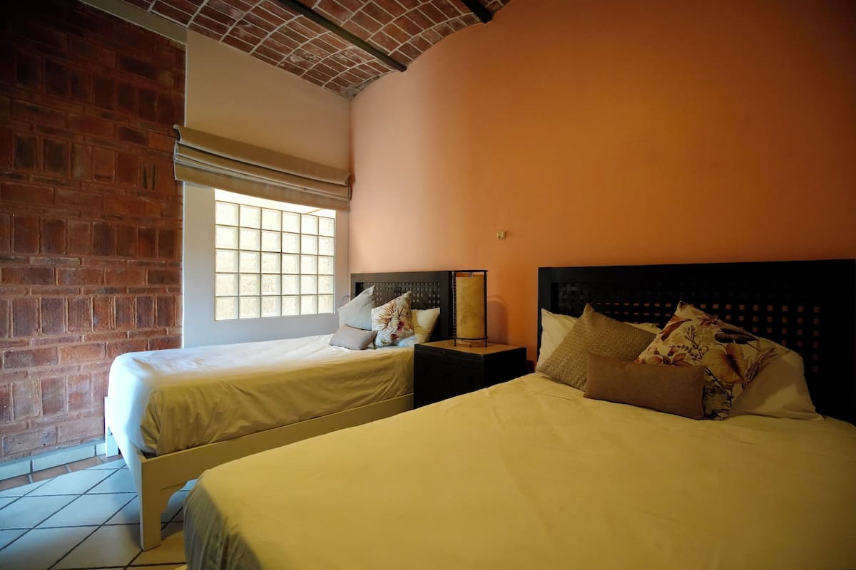 A hotel room with two beds, a brick wall, a window, and a ceiling with exposed beams.