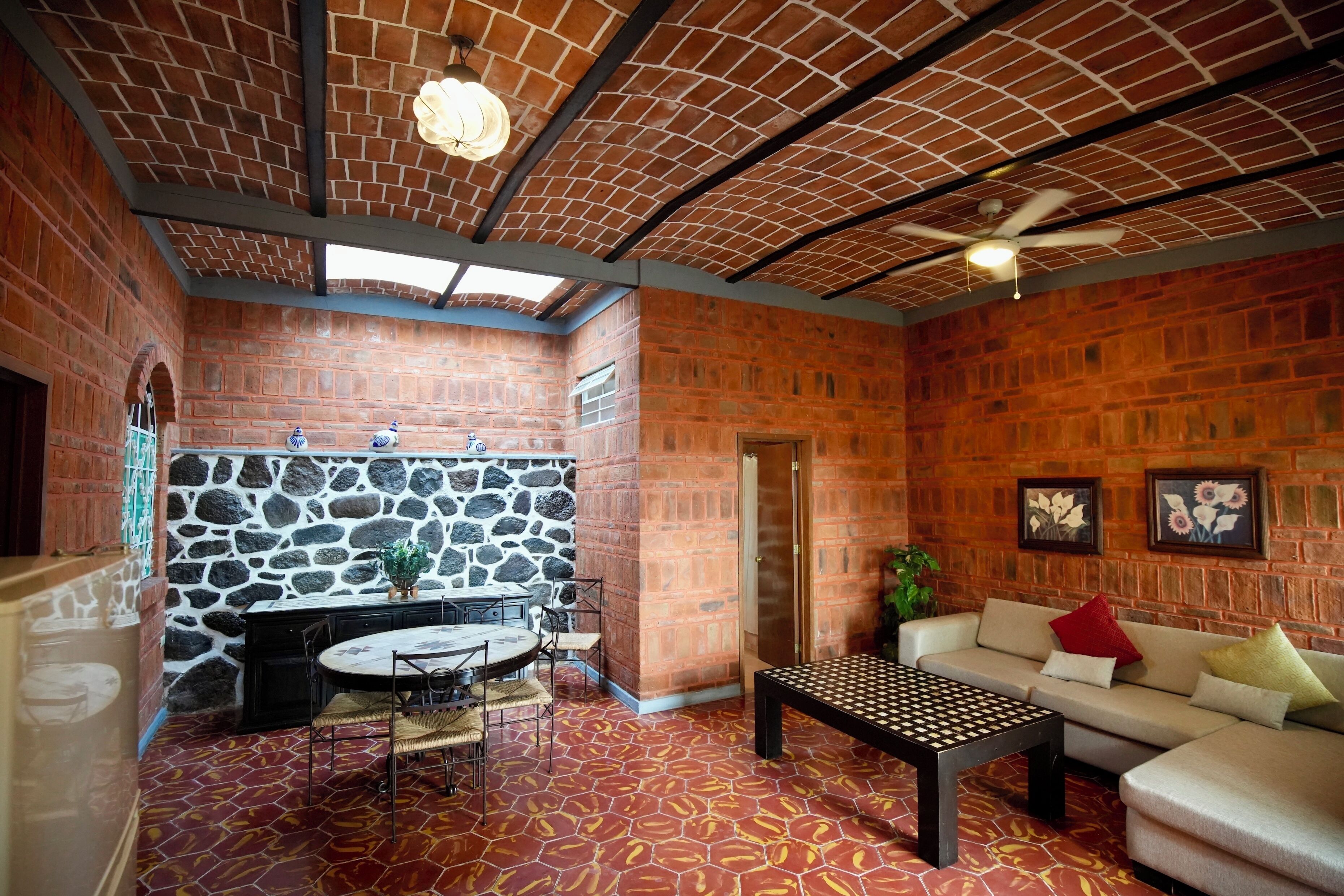 Une pièce avec un mur en briques, un mur en pierre, un ventilateur de plafond, une table avec des chaises, un canapé et un sol à motifs.