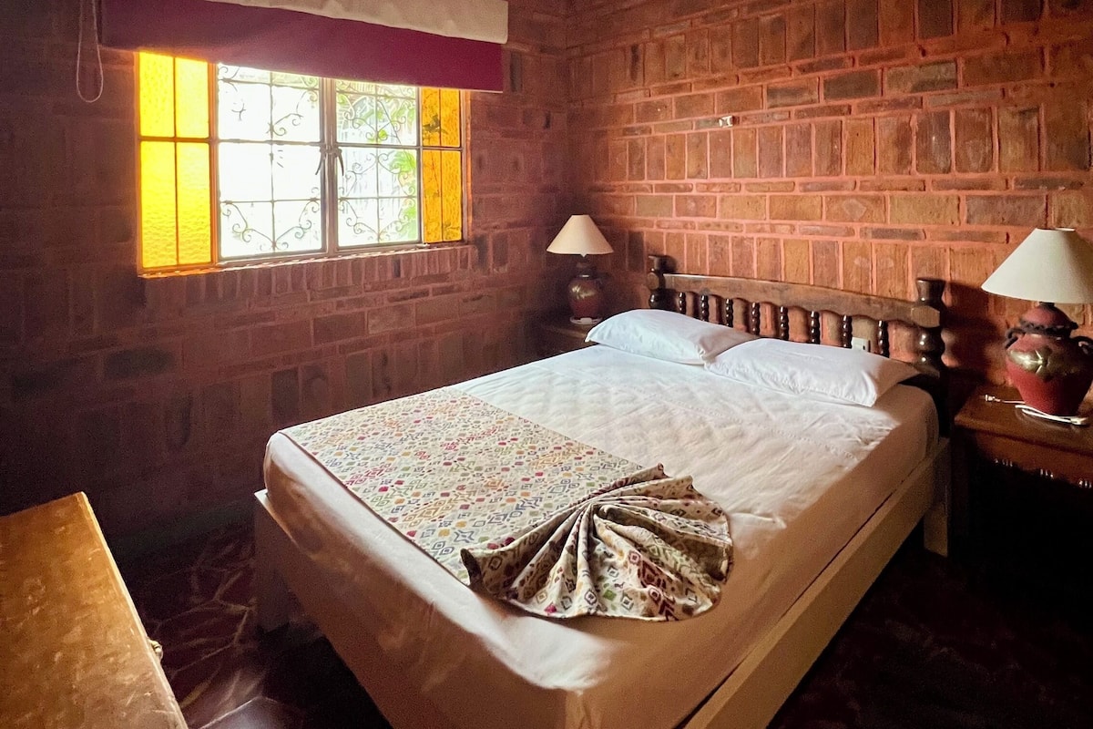 A room with a brick wall, a wooden bed, a ceiling fan, and a window with curtains.