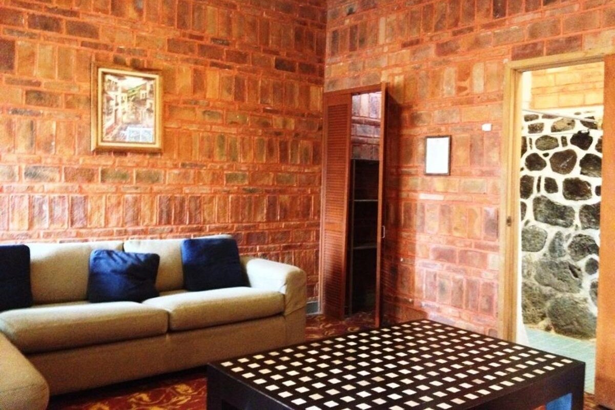 Ein Zimmer mit Backsteinwand, einer Couch mit Kissen, einem gemusterten Tisch und einer Tür zur Steinwand.