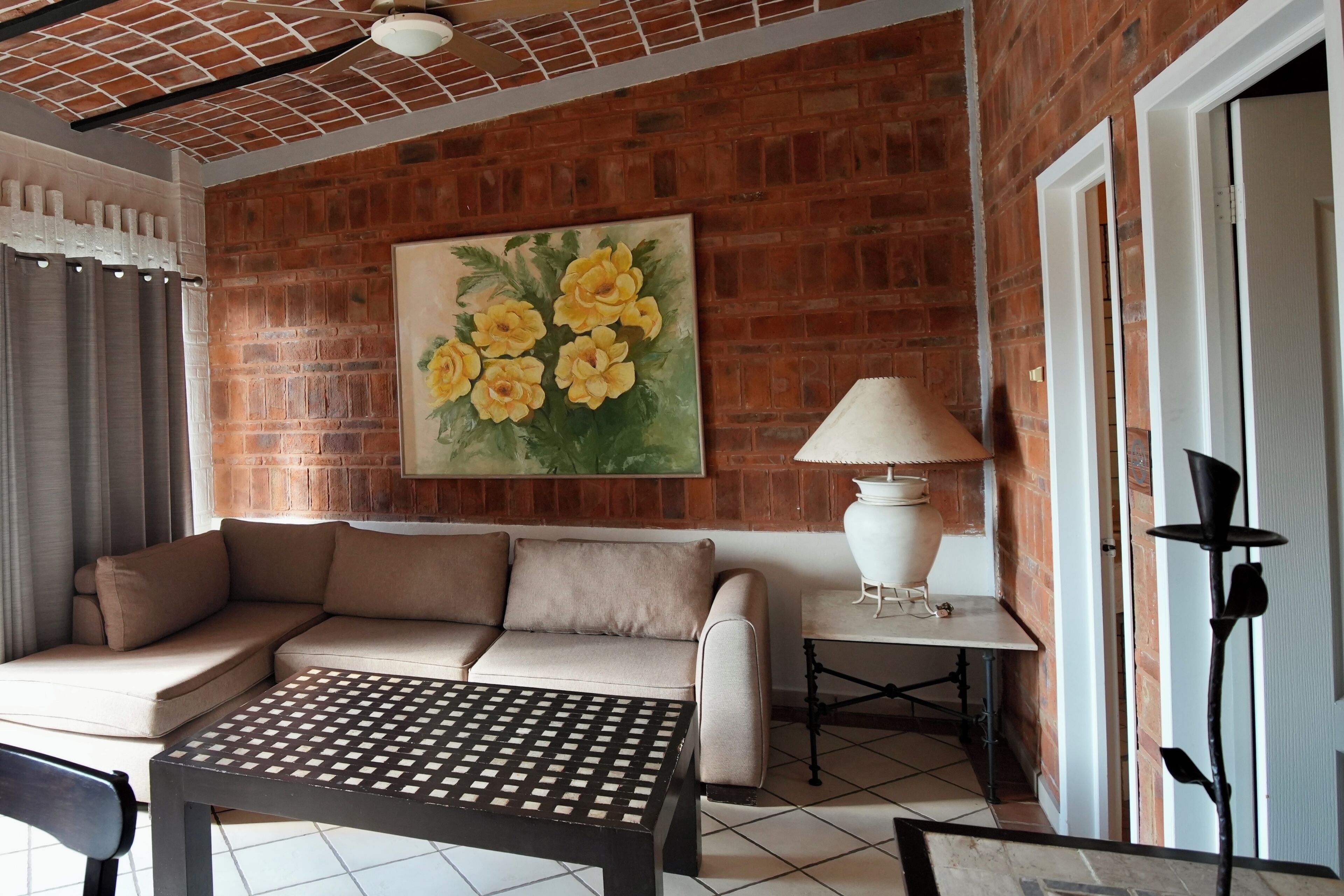 Una sala de estar acogedora con pared de ladrillo, un sofá color beige, una mesa de centro estampada y un cuadro de flores amarillas.