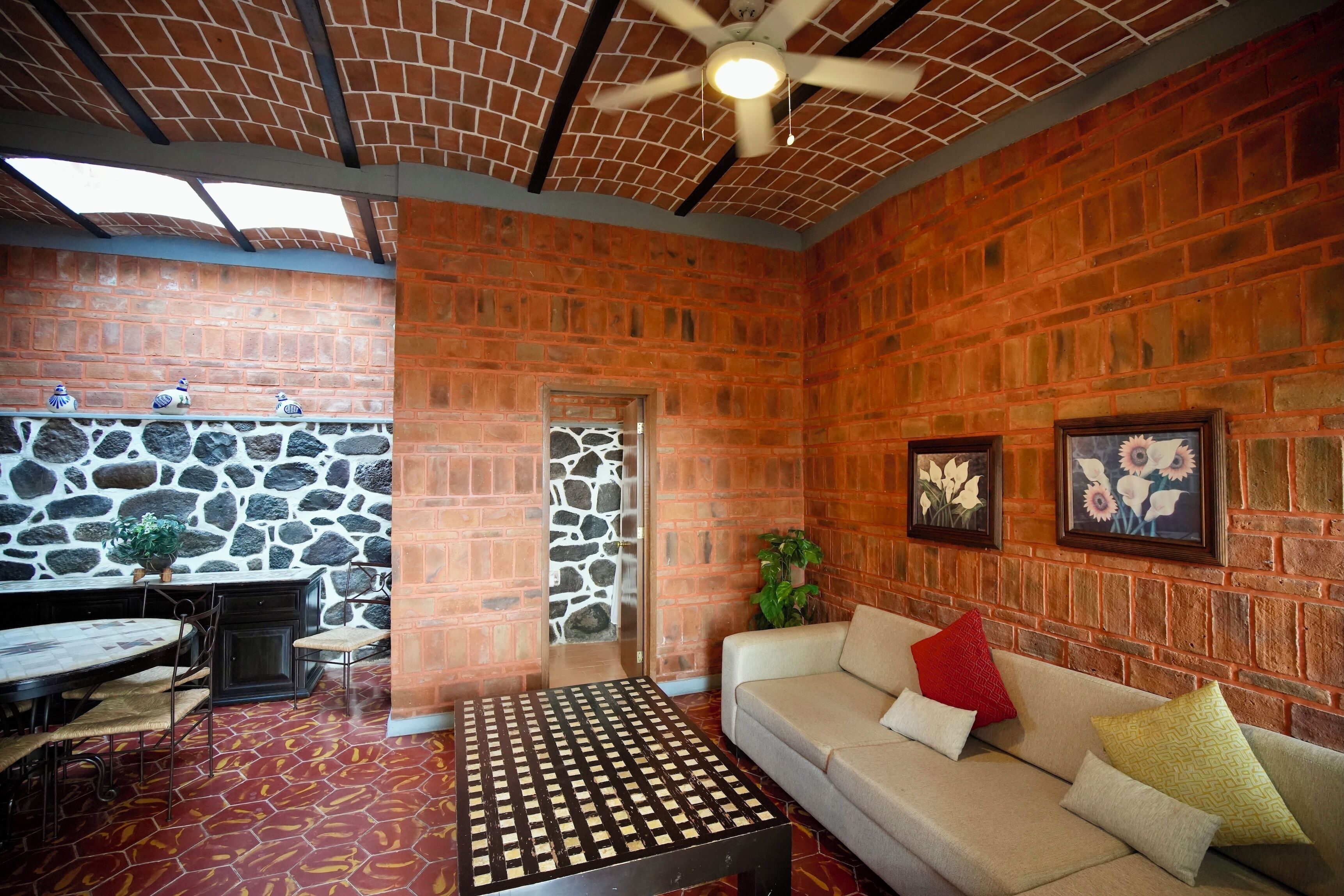 Una habitación con pared de ladrillo, pared de piedra, ventilador de techo, sofá, mesa de centro y una mesa de comedor con sillas.