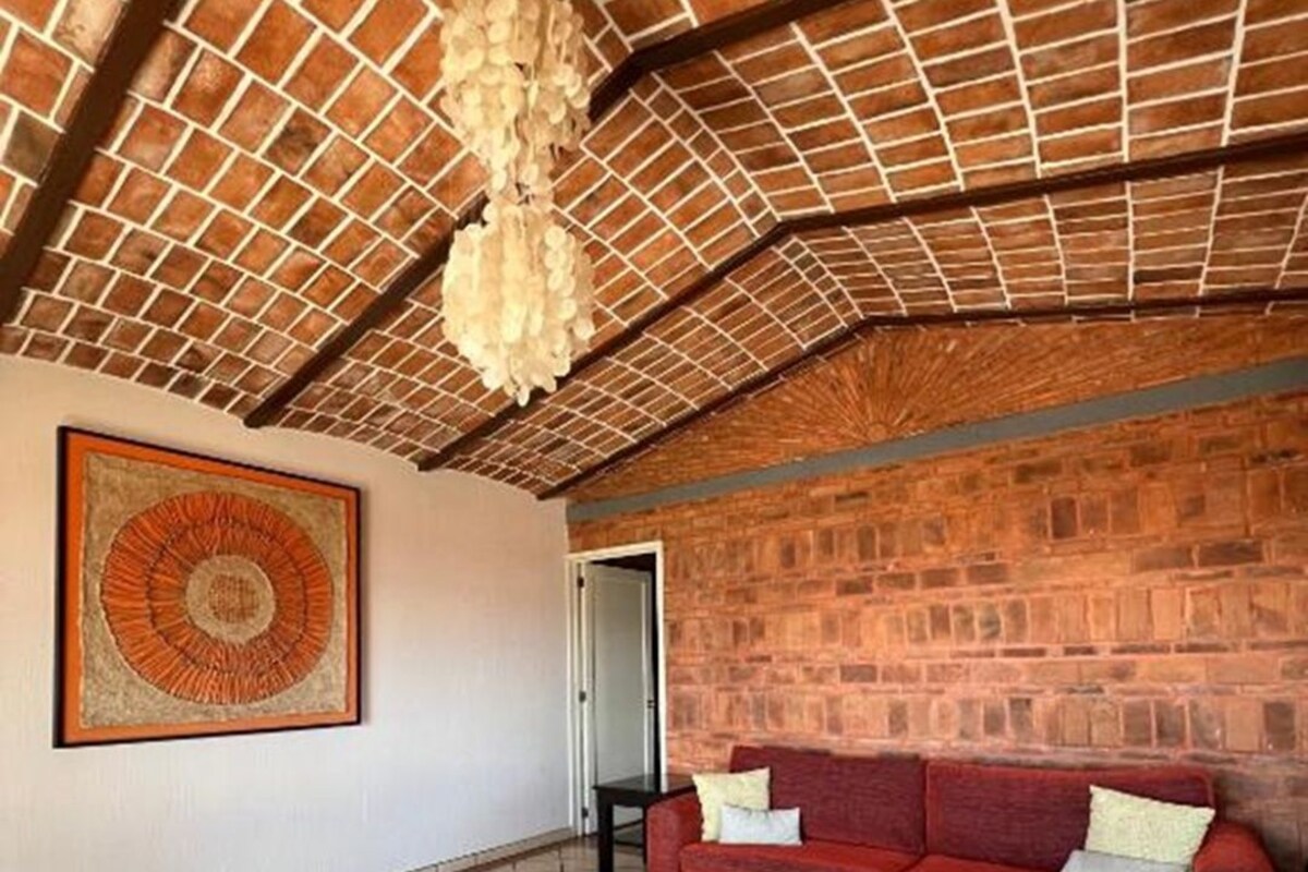 Een woonkamer met een bakstenen muur, een rode bank, een zwarte salontafel en een kamerbreed tapijt met een patroon.