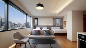 A modern hotel room with a large window offering a city view, a sofa with decorative pillows, a black coffee table, and a bed with a headboard. - Moxy Seoul Insadong (Seoul)