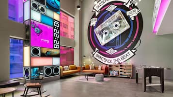 A modern lounge with a retro cassette theme, including a large wall mural, a foosball table, and a cozy seating area with a sofa and ottoman.