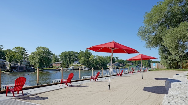 A waterfront deck with red chairs and umbrellas, a wooden walkway, and a river view. - Wasaga Riverdocks Hotel Suites (Wasaga Beach)