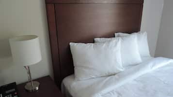 Un lit bien fait, avec du linge de lit blanc, une tête de lit en bois et une table de chevet sur laquelle se trouvent une lampe et un téléphone.
