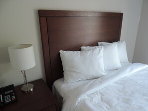 A neatly made bed with white linens, a wooden headboard, and a bedside table with a lamp and a phone. - Wasaga Riverdocks Hotel Suites (Wasaga Beach)