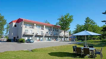 Un hôtel à plusieurs étages, doté d’un toit rouge, d’un espace extérieur aménagé pour s’asseoir et d’un parking.