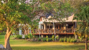 A building with a covered outdoor area, surrounded by trees and grass. - Lilayi Lodge (Lusaka)