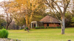 A thatched-roof house surrounded by a grassy area and trees. - Lilayi Lodge (Lusaka)