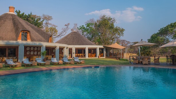 A pool area with lounge chairs and a thatched-roof building. - Lilayi Lodge (Lusaka)