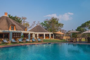 A pool area with lounge chairs and a thatched-roof building. - Lilayi Lodge (Lusaka)
