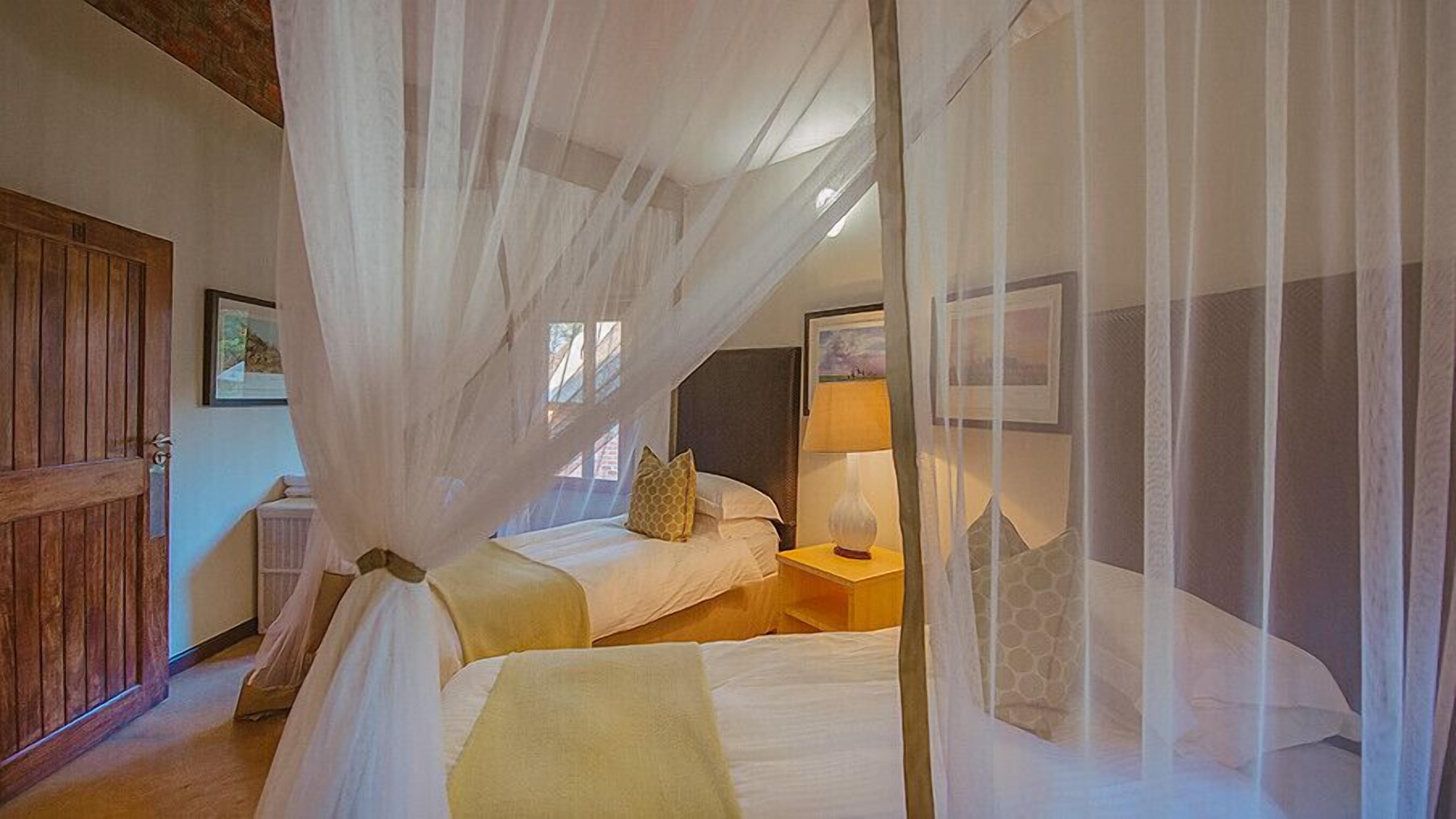 A bedroom with a bed under a canopy, a nightstand with a lamp, and a wooden door.