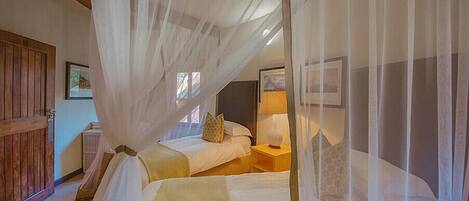 A bedroom with a bed under a canopy, a nightstand with a lamp, and a wooden door.