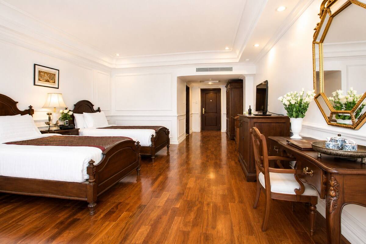 Een hotelkamer met twee houten bedden, een bureau met stoel, een grote spiegel en een televisie.