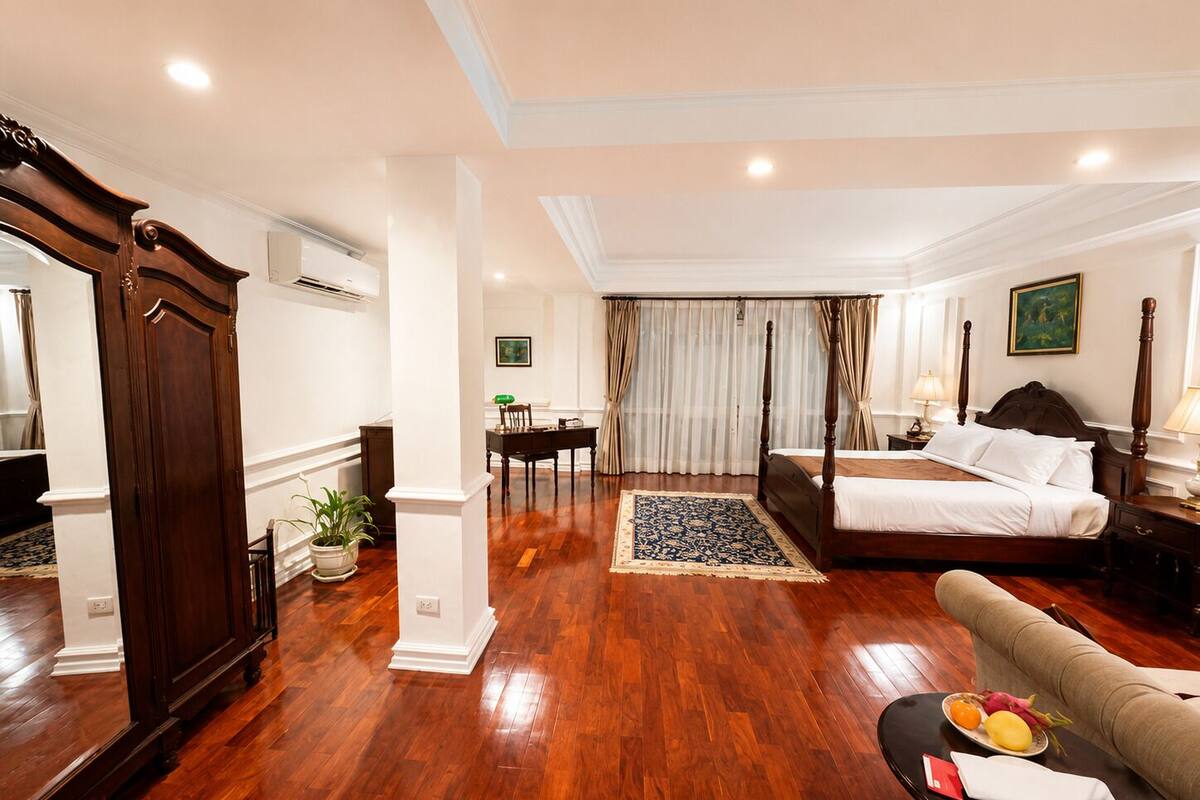 Een hotelkamer met een groot bed, een zithoek met een tafel en stoelen, een eettafel en een grote spiegel.