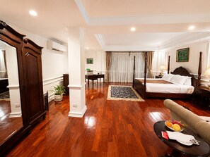 Una habitación de hotel con una cama grande, una zona de estar con una mesa y sillas, una mesa de comedor y un espejo grande.