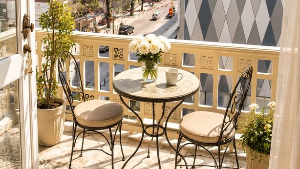 Uma varanda com piso estampado, duas cadeiras, uma mesa e um vaso com planta.