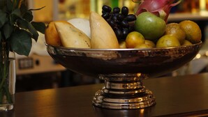 Uma fruteira sobre uma mesa, com um vaso de flores à esquerda.