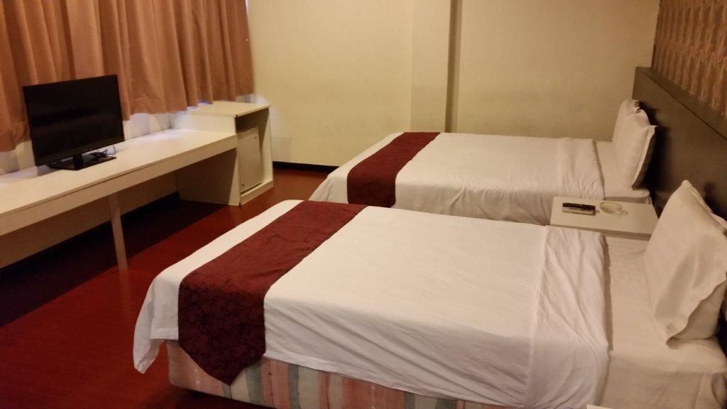 A hotel room with two beds, a desk with a television, and a small table with a phone.