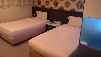 A hotel room with two single beds, a nightstand with a telephone, and a wall with a floral pattern.