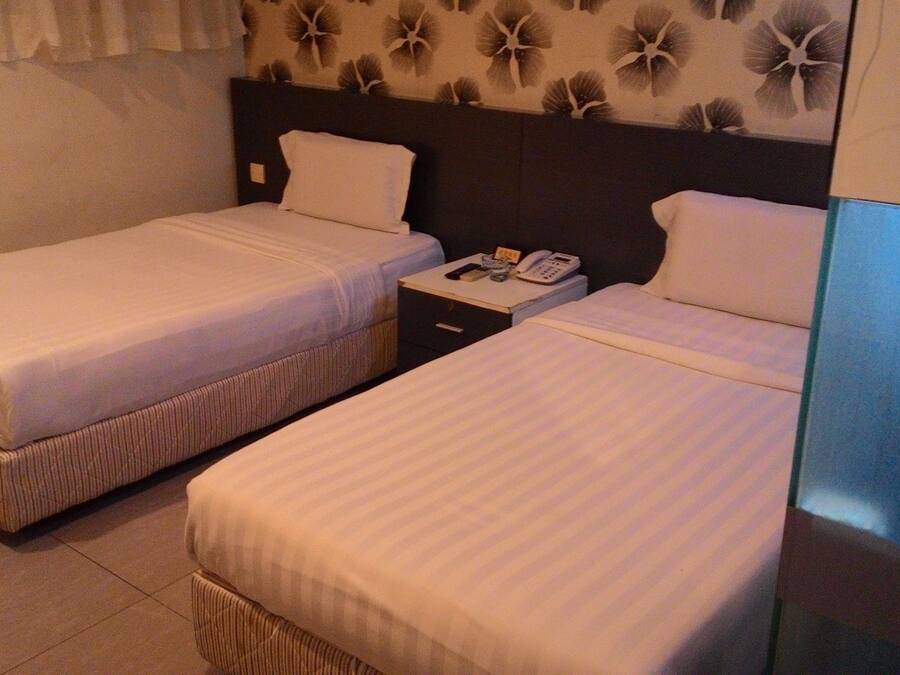 A hotel room with two single beds, a nightstand with a telephone, and a wall with a floral pattern.