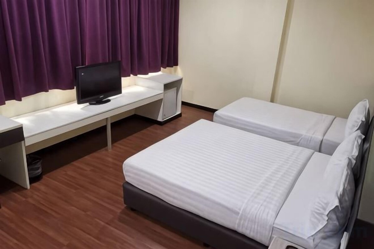 Habitación de hotel con dos camas, un escritorio y una computadora, y cortinas moradas.