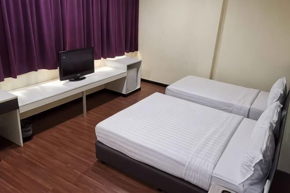 A hotel room with two beds, a desk with a computer, and purple curtains.