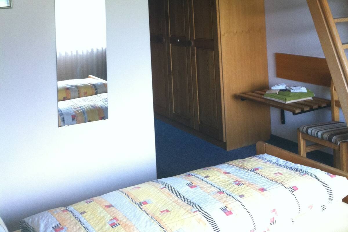 Ein Zimmer mit einem Stockbett, einer Holzleiter, einem Kleiderschrank und einem kleinen Tisch mit Stuhl.