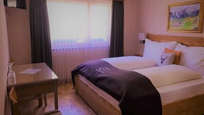 A hotel room with a bed, a small desk, and a window with curtains.