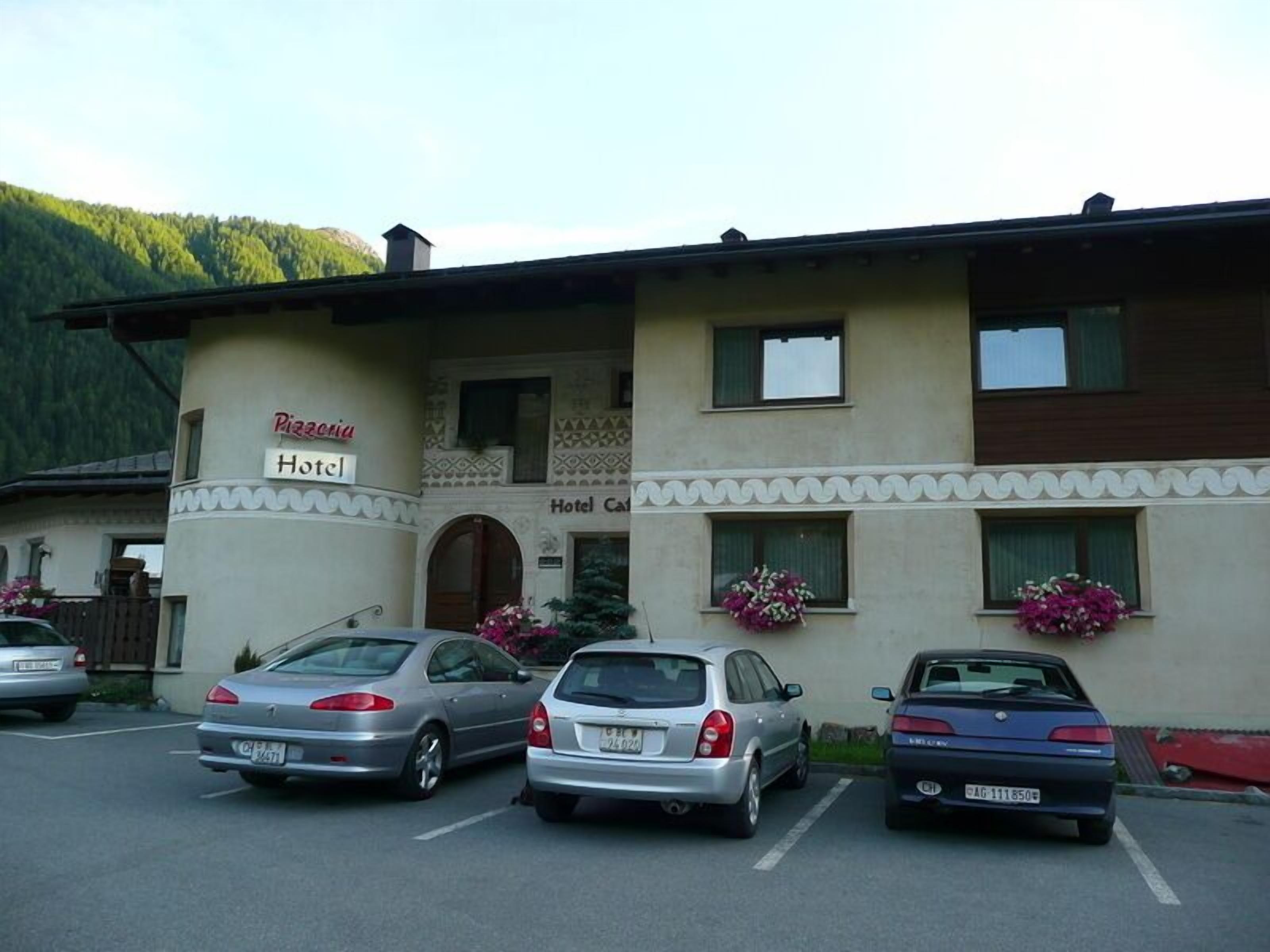 A hotel with a sign indicating it offers pizza and a parking lot with three cars.