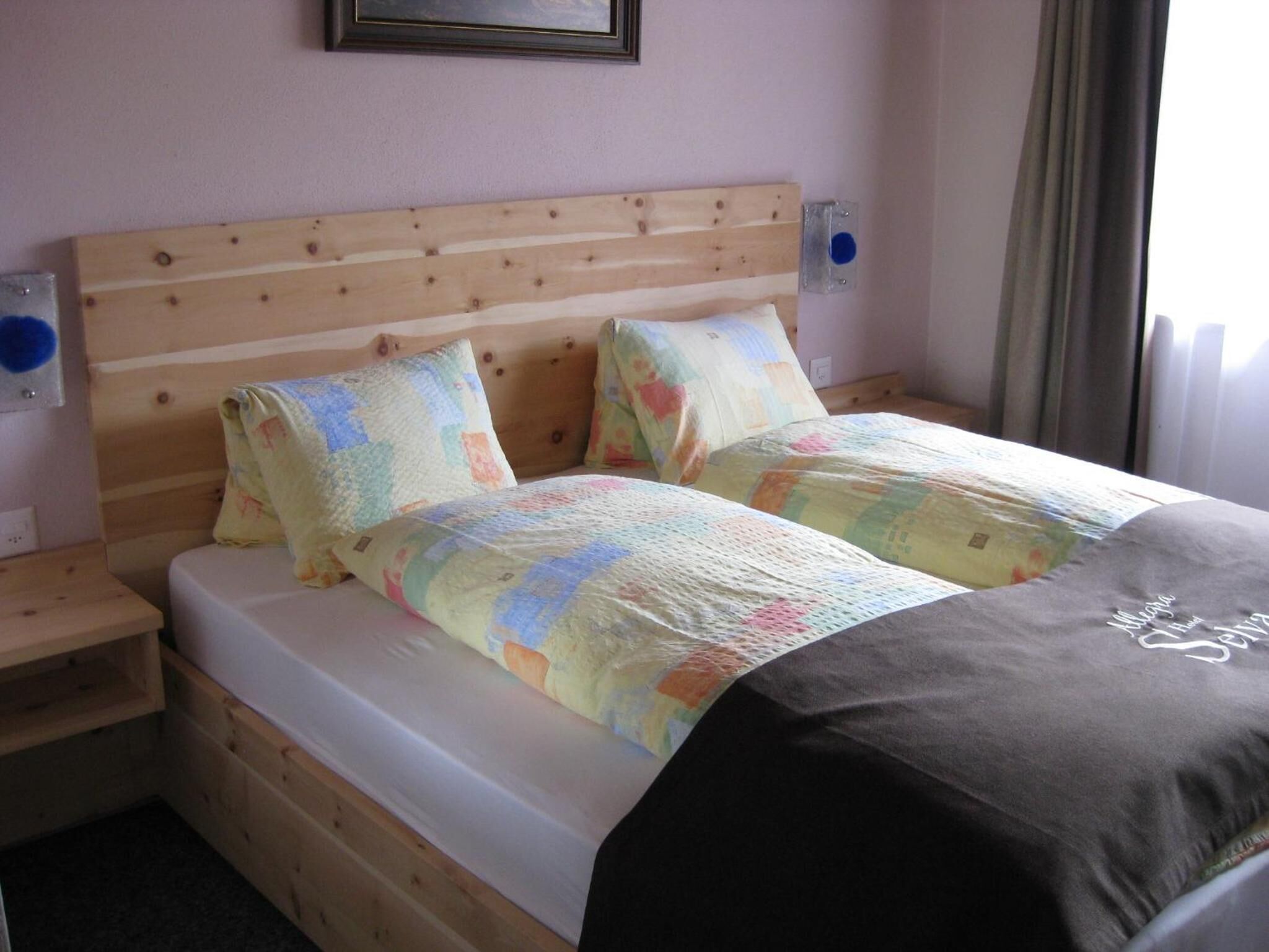 Een tweepersoonsbed met een houten hoofdbord, twee nachtkastjes en een bedlampje.