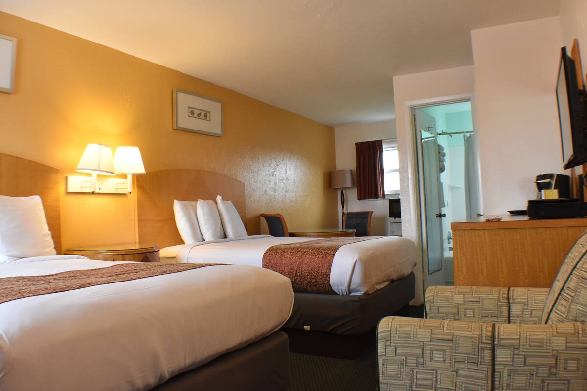 A hotel room with two beds, a desk, a chair, and a television.