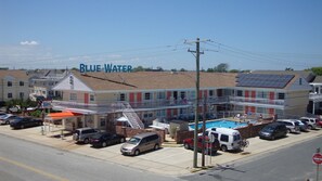 A building with a swimming pool, a covered outdoor seating area, and a sign reading "BLUE WATER". - Blue Water Motel (Wildwood Crest)