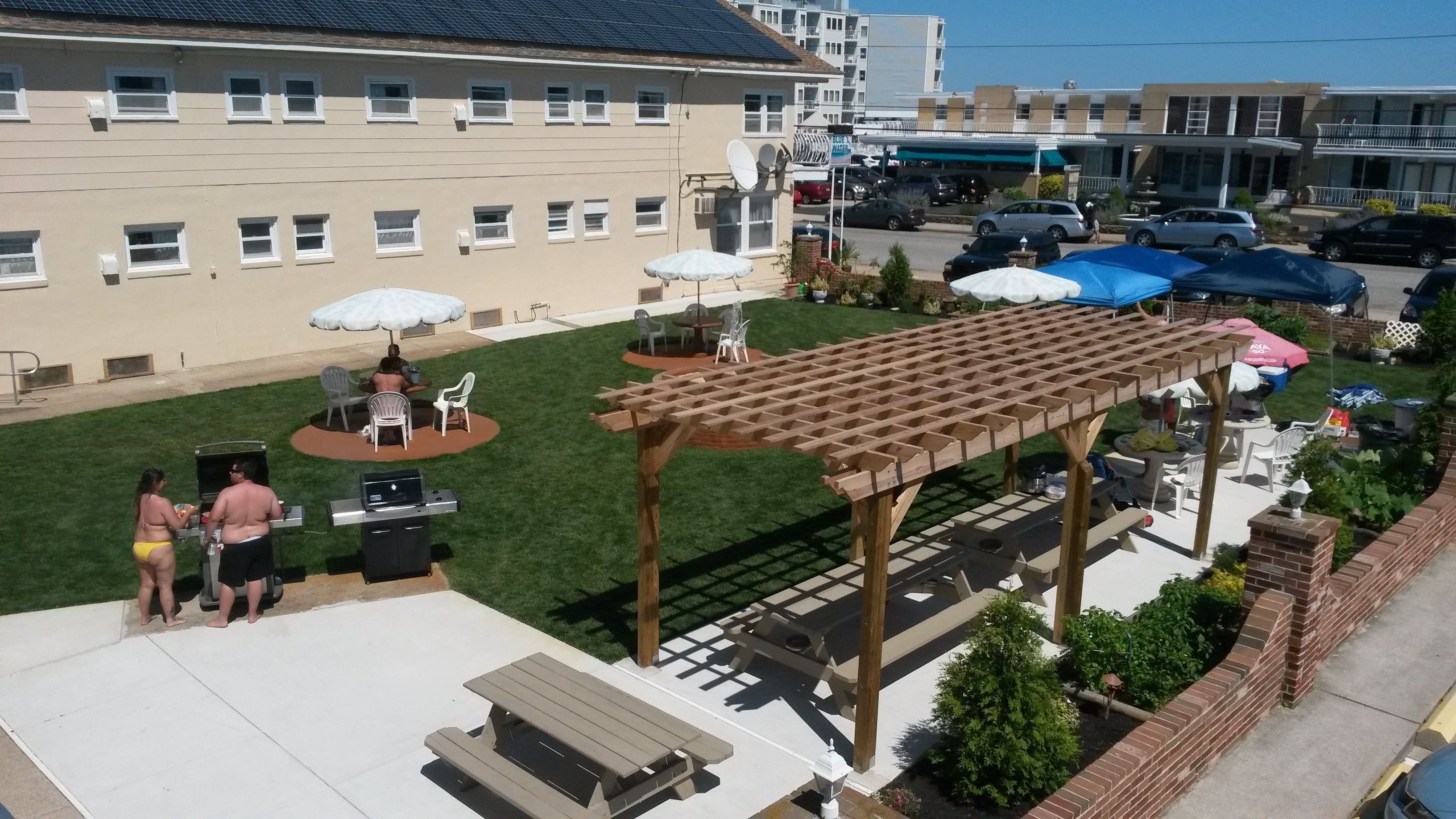 A patio area with a wooden pergola, outdoor seating, and a barbecue grill.