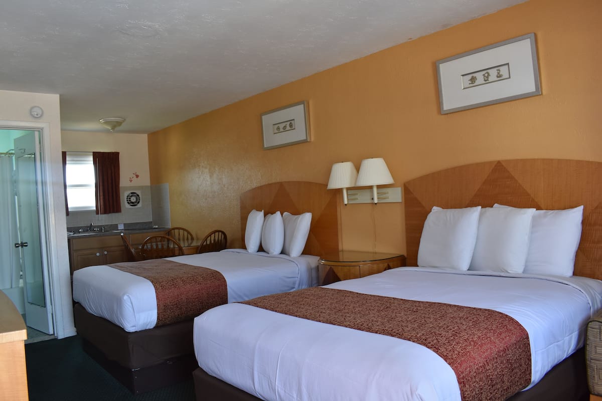 A hotel room with two beds, a small kitchenette, a bathroom, and a dining area.