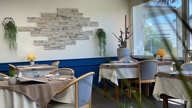 A restaurant interior with tables set for dining, a stone wall decoration, and hanging plants. - Hotel fontaine morlaix  (Morlaix)