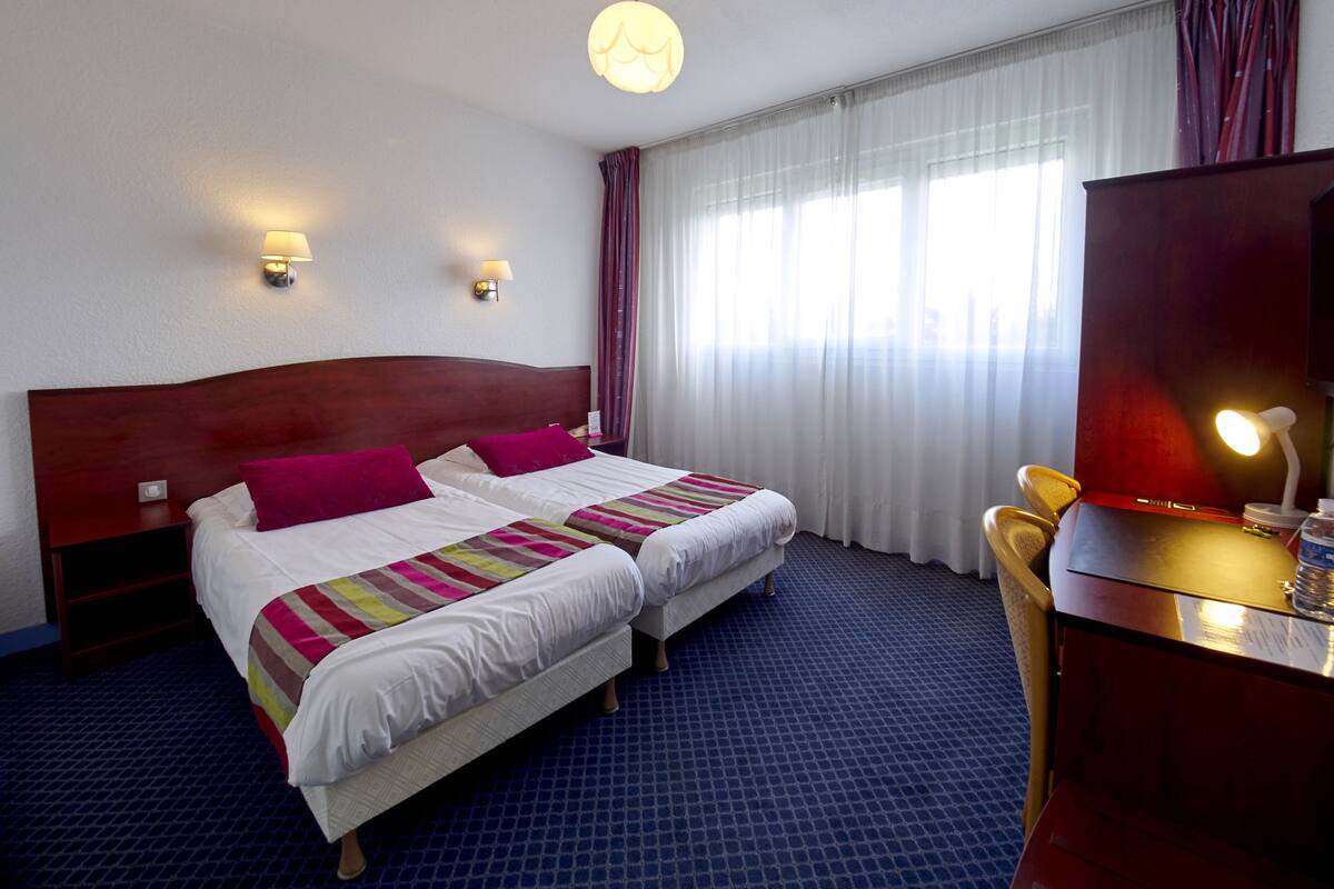 A hotel room with two beds, a desk, a chair, and a large mirror.