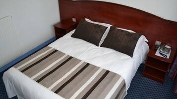 A neatly made bed with a striped bedspread, a wooden headboard, and a bedside table with a telephone and a notepad.