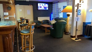 A cozy lounge area with wooden bar stools, green upholstered chairs, a wooden table, and a television mounted on the wall. - Hotel fontaine morlaix  (Morlaix)